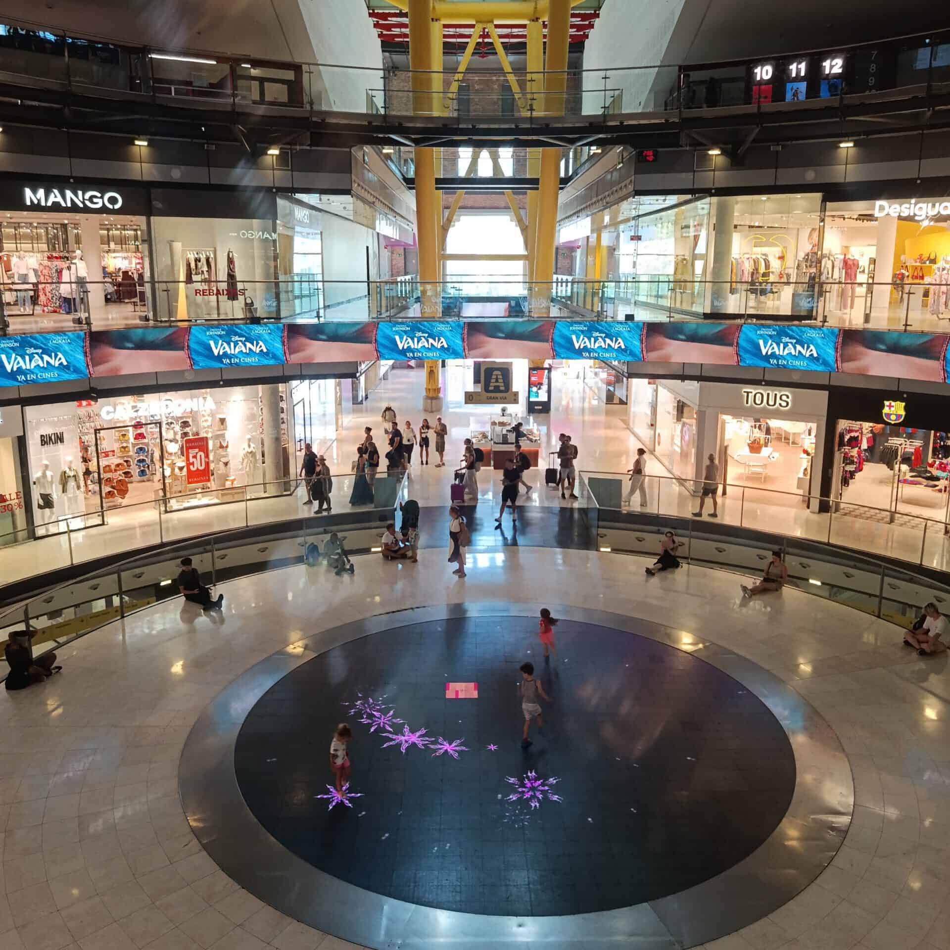Modern shopping mall interior with stores and shoppers, IWY Tour Guide.