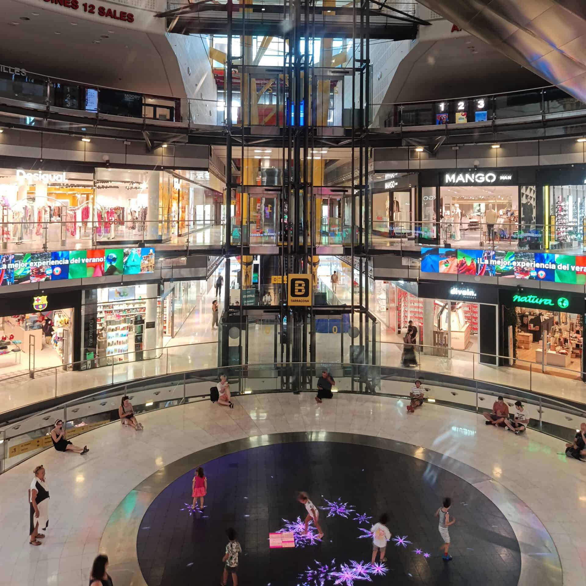 Interior view of a multi-level shopping mall with stores and escalators.